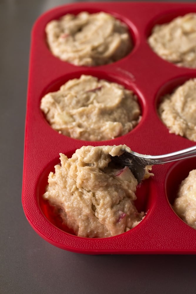 scooping muffin batter into a red silicone muffin tin with a spoon