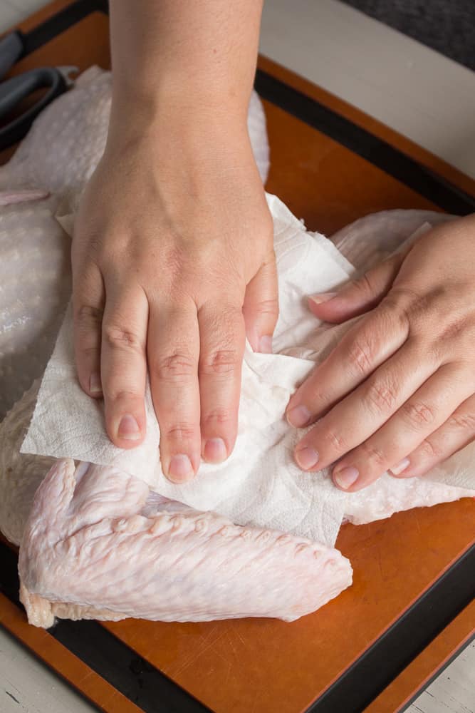 A pair of hands drying off a raw turkey with paper towels.