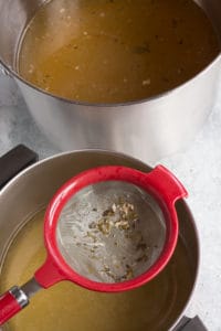 a fine mesh strainer over a pot of turkey stock with the unrefined stock in a pot next to it