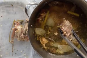 removing bones and veggies from a large pot of turkey broth into a container on the side