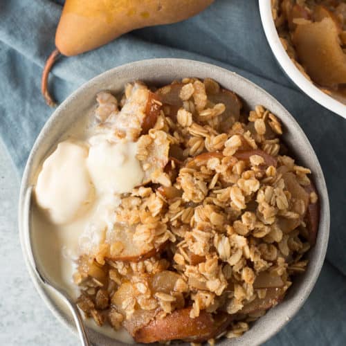 bowl of gluten free pear crisp with melted ice cream and a spoon
