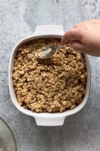 spreading out oat topping onto pears in a white baking dish with a spoon