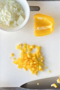 bell pepper being diced with a bowl of diced onion to the side