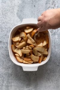 mixing cooked pears in a white square baking dish with a spoon