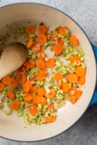 chopped carrots and celery cooking in a large pot with a wooden spoon