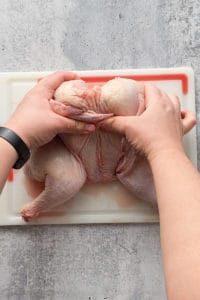 flattening a raw spatchcock chicken on a cutting board