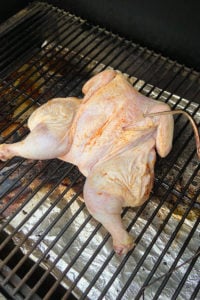a raw chicken smoking on a Traeger grill with a temperature probe in it