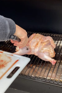 placing a raw chicken on a wood pellet grill to smoke