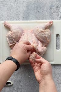 putting dry brine seasoning under the skin of a raw chicken