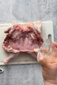 sprinkling seasoning on the underside of a raw chicken