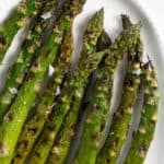 Top down shot of grilled asparagus on a white platter with finishing salt sprinkled on top.