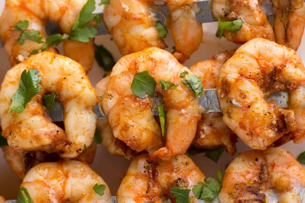 Close up of grilled shrimp on metal skewers laying on a white platter.