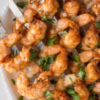 grilled shrimp skewers on a white platter with herbs and a lime
