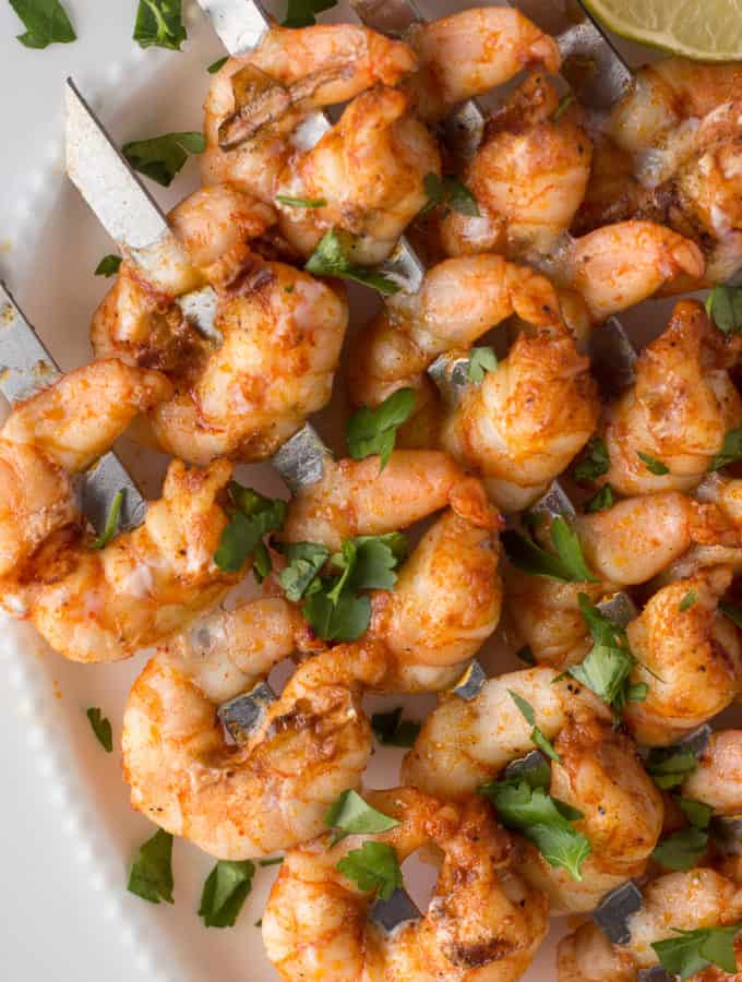 grilled shrimp skewers on a white platter with herbs and a lime