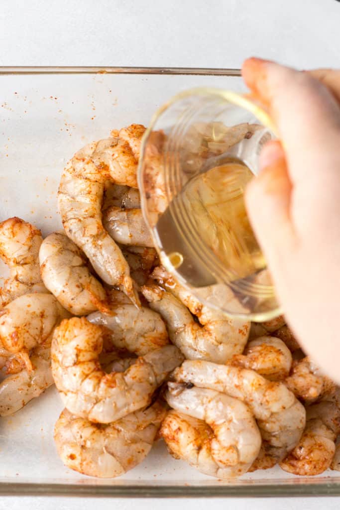 pouring oil over seasoned raw shrimp