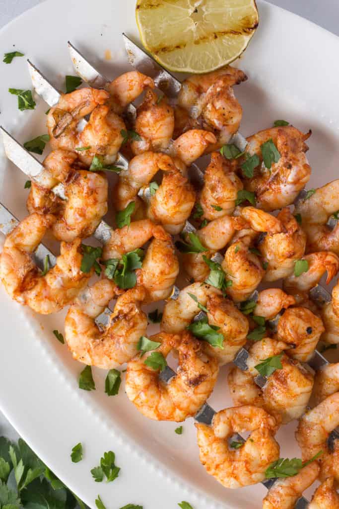 grilled shrimp skewers on a white platter with green garnishes