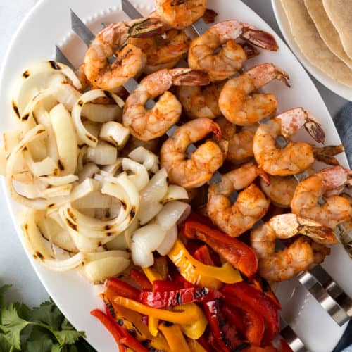 top down shot of a white platter with grilled shrimp on skewers, grilled onions and grilled bell peppers