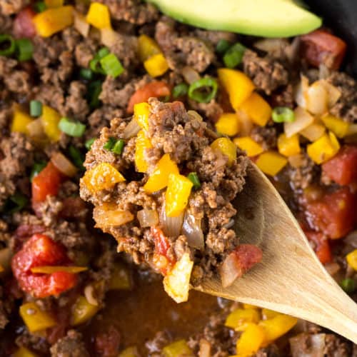 top down shot of a wooden spoon digging mexican ground beef out of a pan