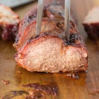 head on shot of a medallion of smoked pork tenderloin with a meat fork sticking out of the top.