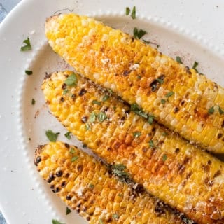 top down shot of grilled corn on the cob with toppings on a white platter