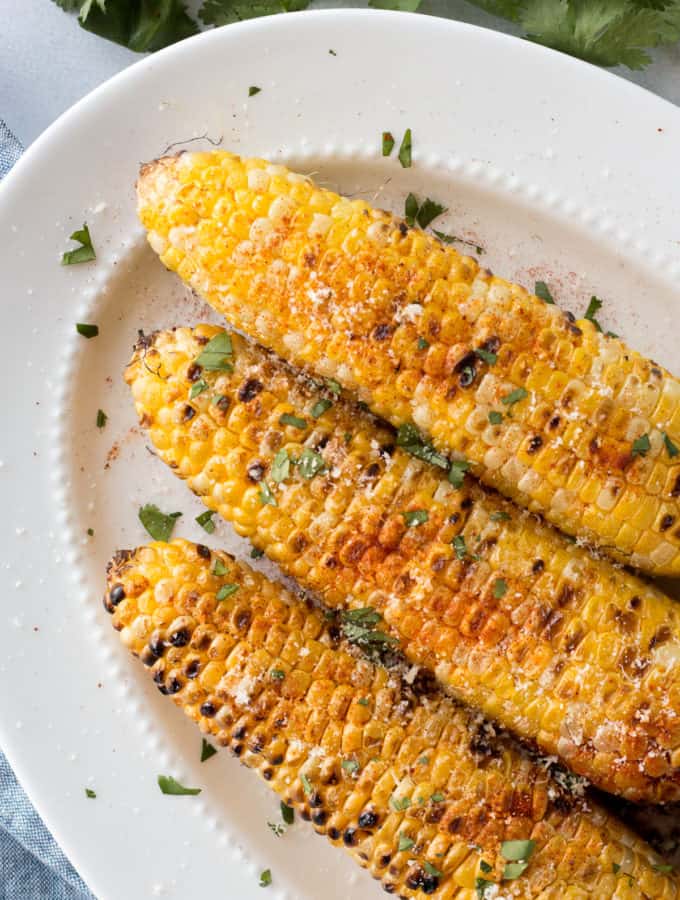 top down shot of grilled corn on the cob with toppings on a white platter