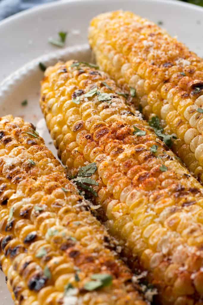 grilled sweet corn with paprika, parmesan, butter, and chopped cilantro on it