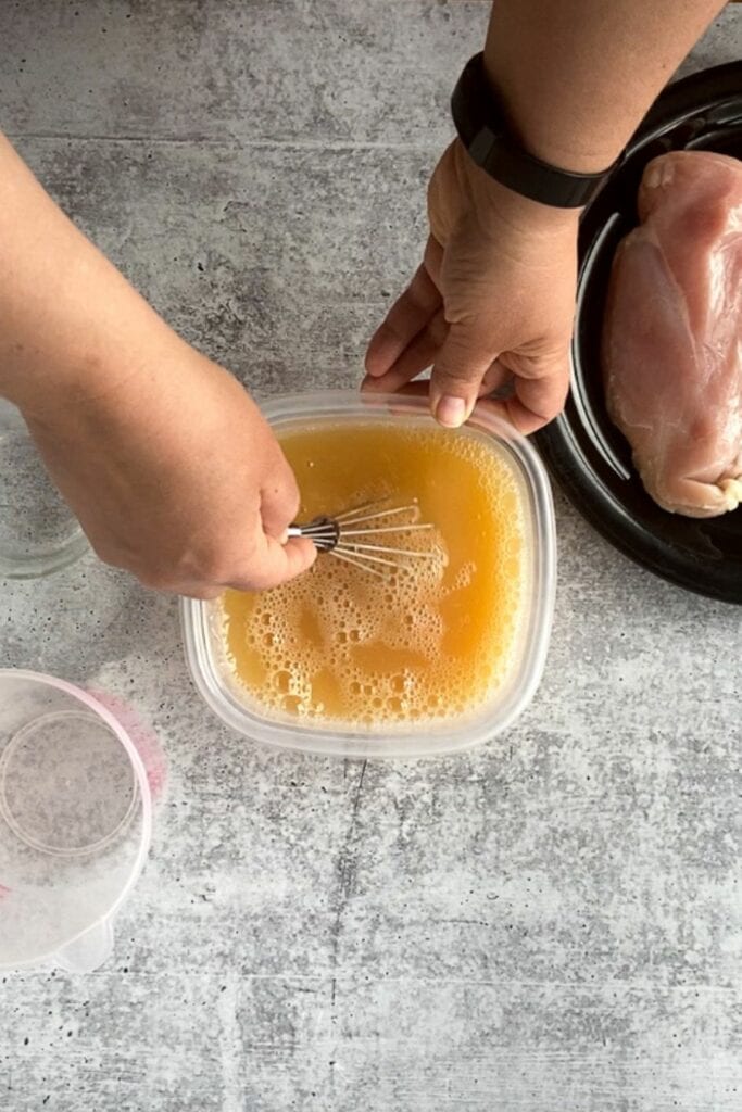 Top down shot of hands whisking an apple juice brine in a square plastic container on a gray background.