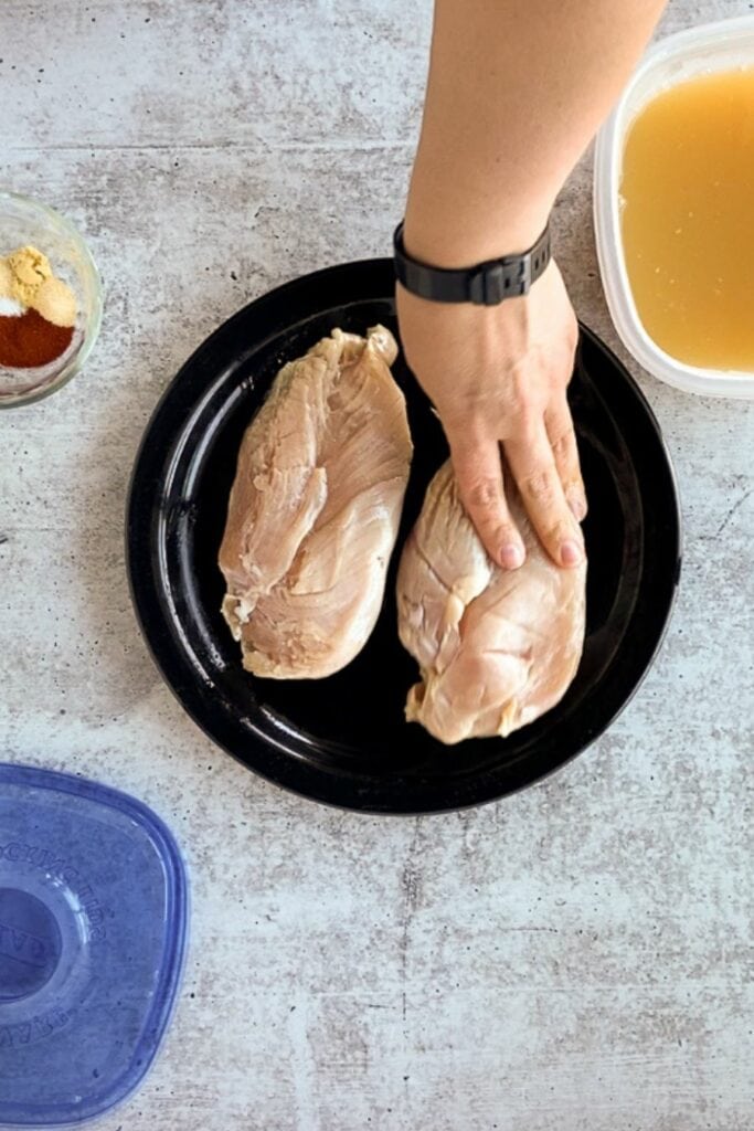 Top down shot of a hand rubbing oil on brined raw chicken breasts on a black plate.