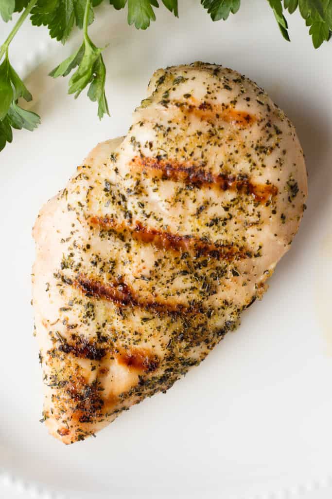 top down shot of a whole grilled greek chicken breast on a white cutting board