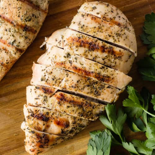 top down shot of greek grilled chicken breast on a cutting board with parsley and a knife