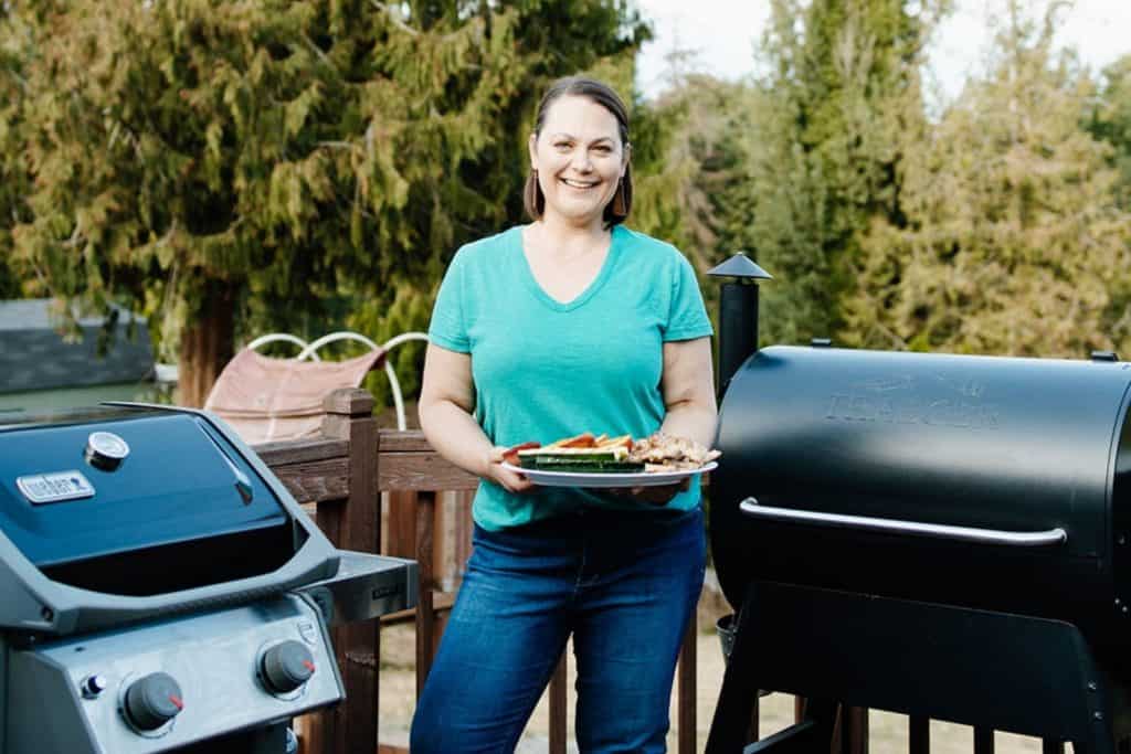 Taryn Solie next to two grills holding a platter of grilled food