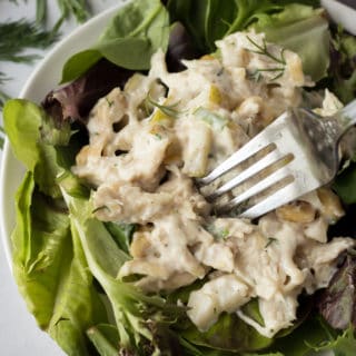 a fork pressing into some pear chicken salad on a plate with mixed greens