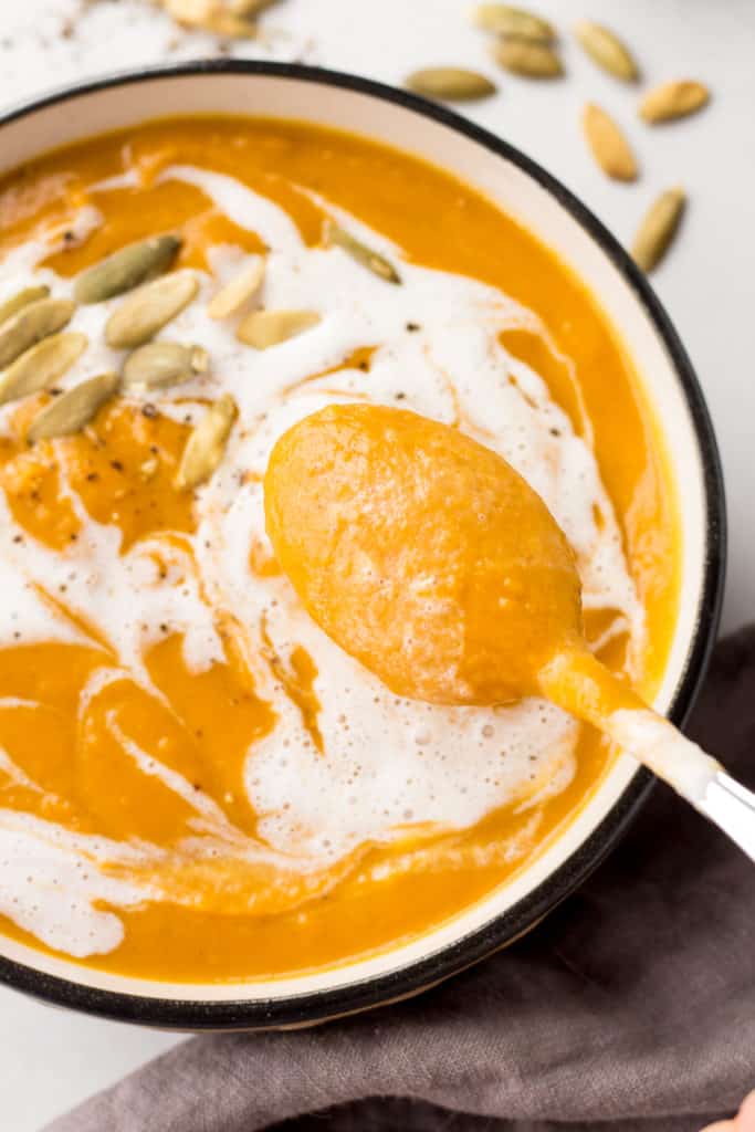 close up of a soup dipping into a bowl with pumpkin sweet potato soup.