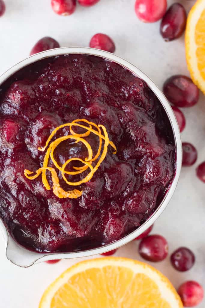close up of gluten free cranberry sauce in a small grey bowl with fresh cranberries and orange slices surrounding it.