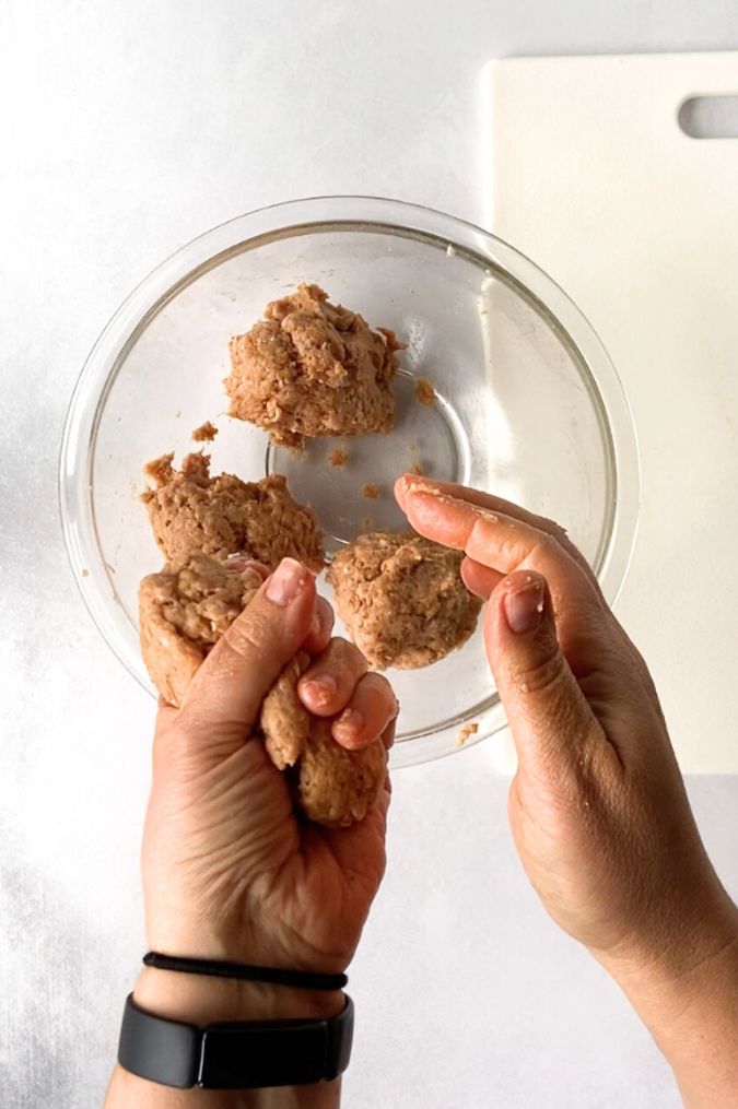 Top down shot of two hands squishing a ground turkey mixture and separating it into four equal portions in a large glass bowl.