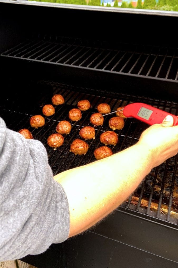 A hand checking the temperature of smoked turkey meatballs with a meat thermometer, with the temperature reading 165F.