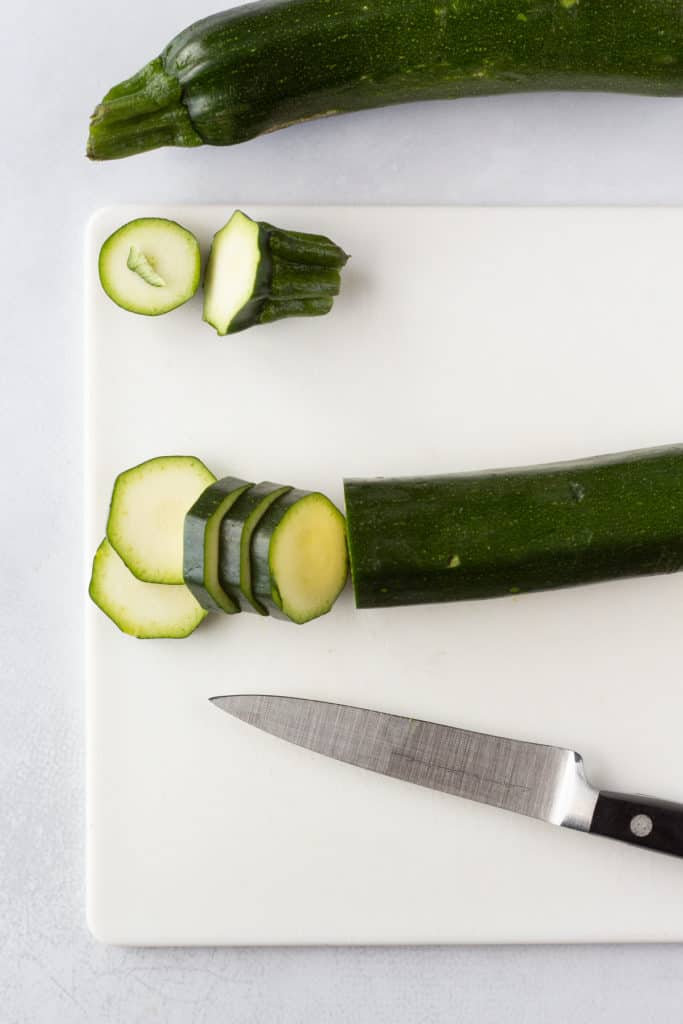 zucchini being sliced on a white cutting board