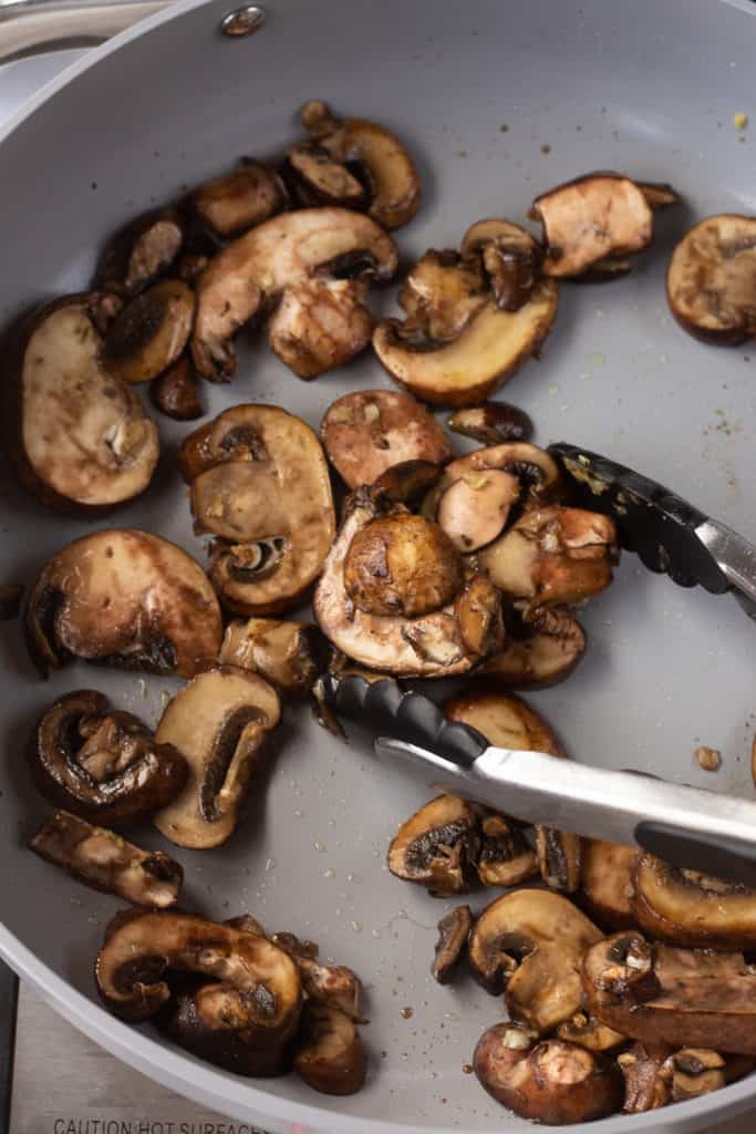 sliced mushrooms being cooked in a gray pan.