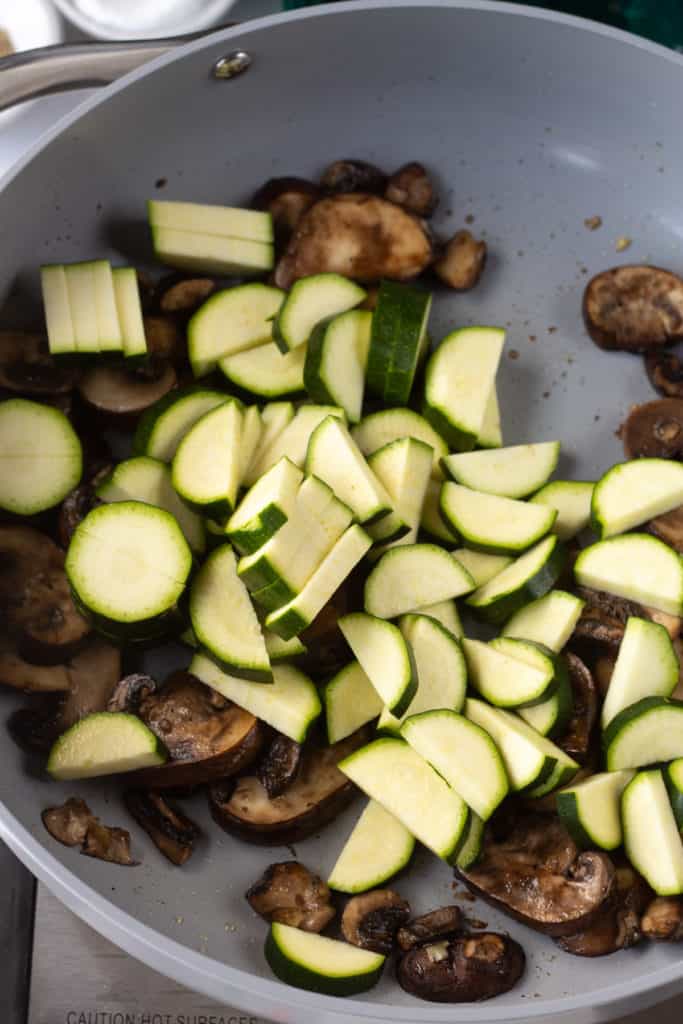 sliced and cut zucchini in a pan with partially cooked sliced mushrooms.