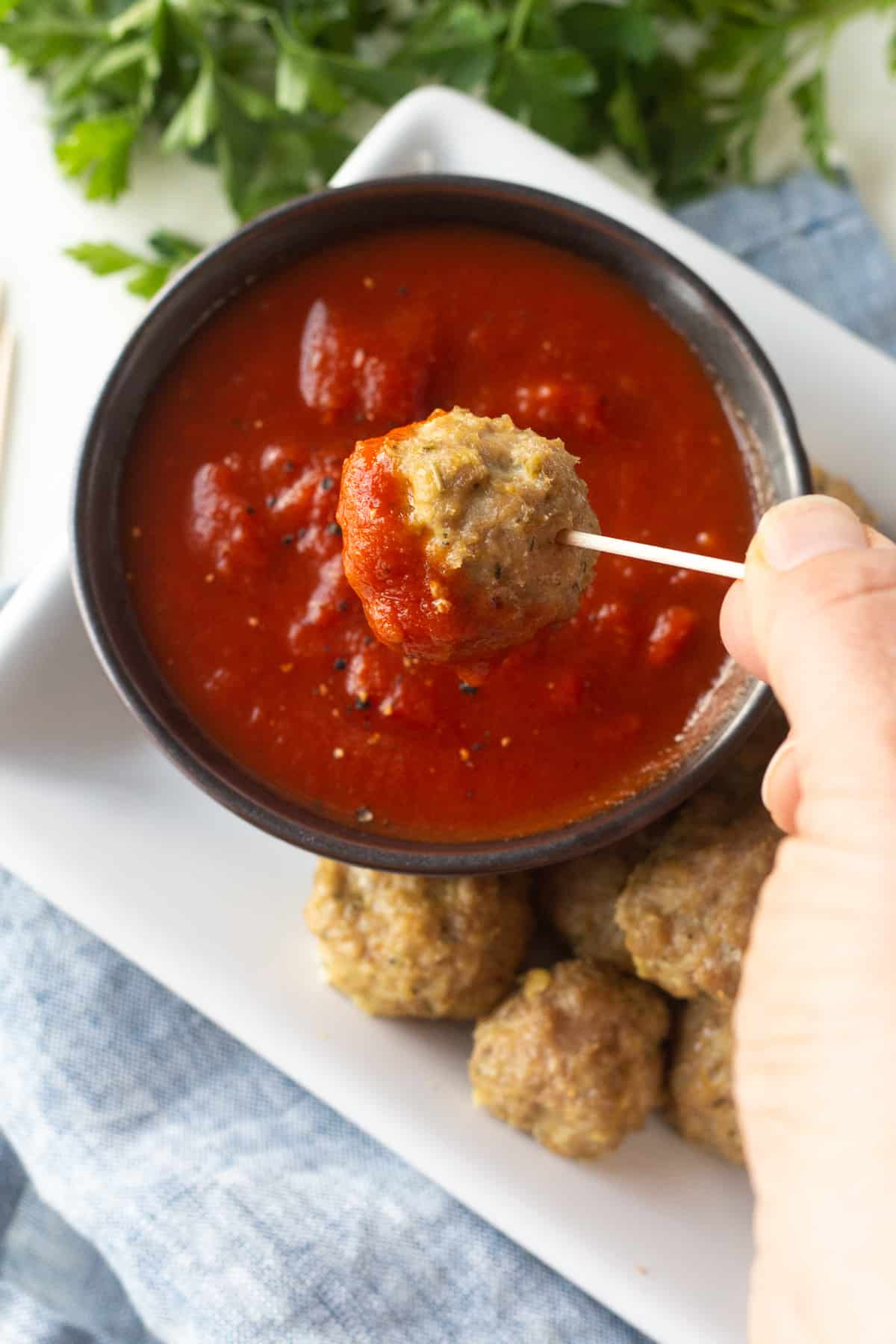 Close up of a turkey meatball with marinara sauce on it held by a toothpick over a bowl of sauce next to other meatballs.