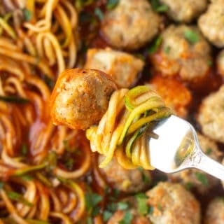 close up of a fork with a turkey meatball and zucchini noodles in marinara sauce on it.