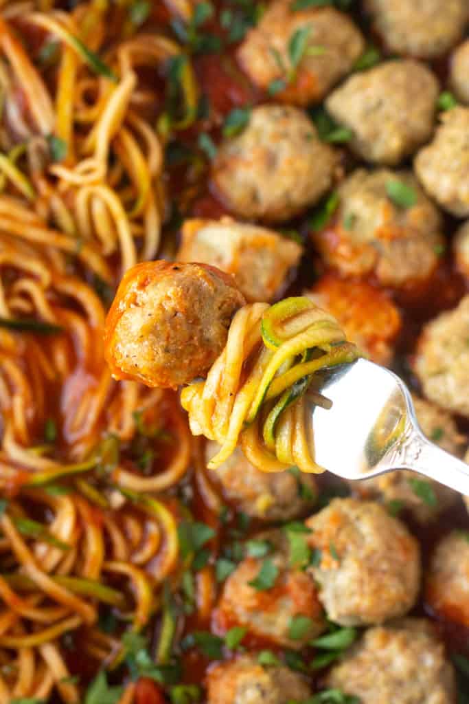 Close up of a fork with a turkey meatball and zucchini noodles in marinara sauce on it.