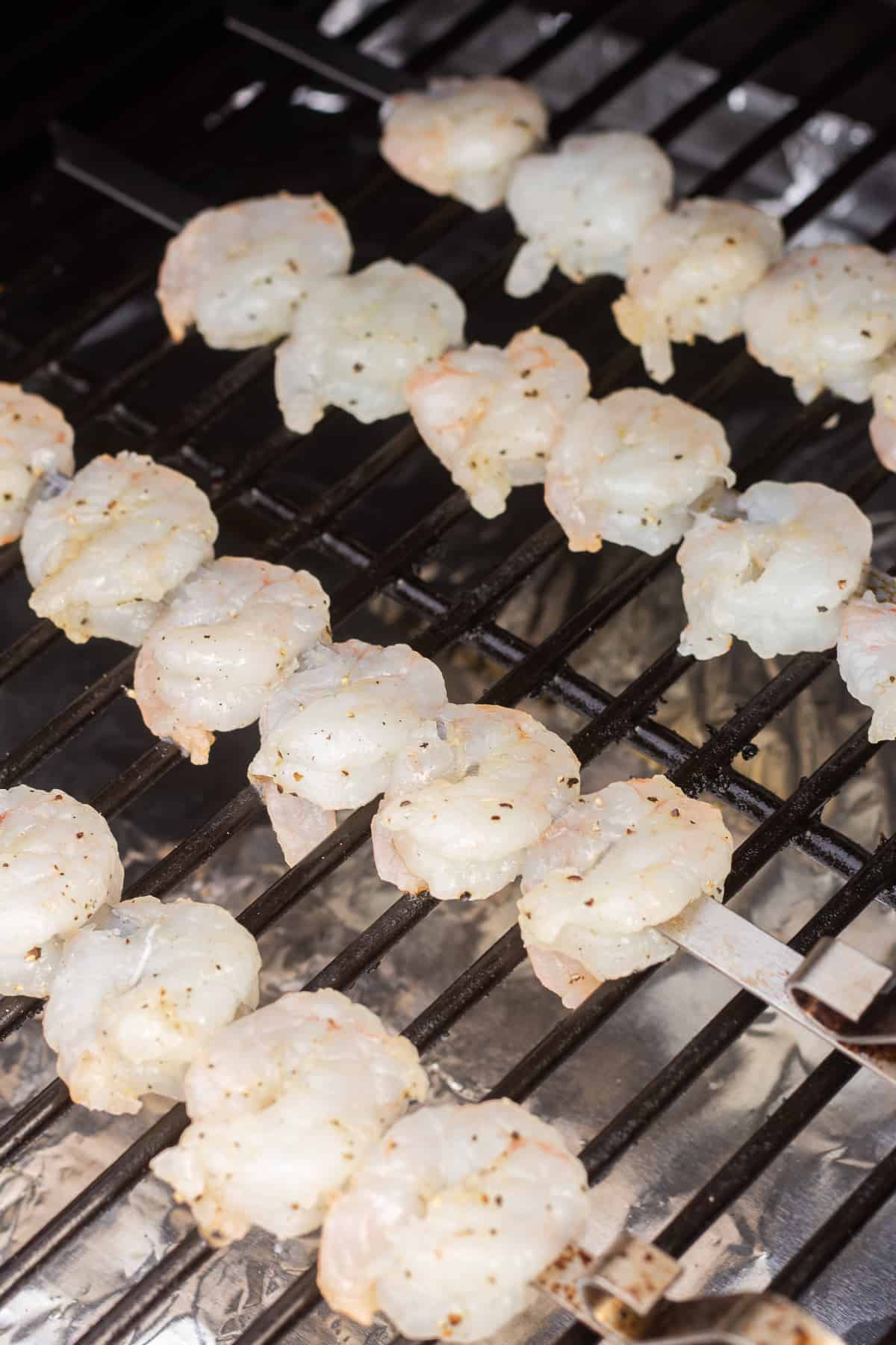 Raw shrimp on metal skewers on grill grates.