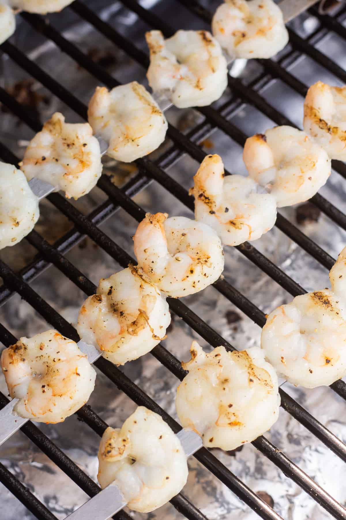 Cooked shrimp on metal skewers on a grill.