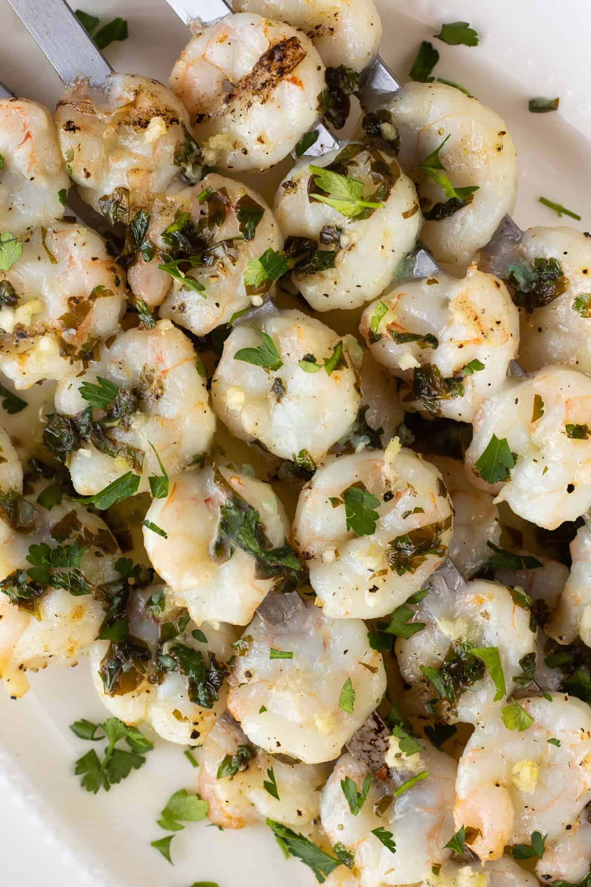 Grilled garlic shrimp on metal skewers piled onto a white platter.