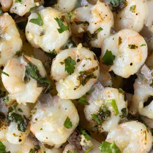 close up of grilled garlic shrimp on metal skewers on a white platter.