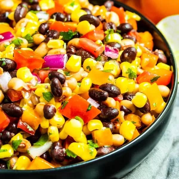 Close up of cowboy cavier with corn, black beans, tomato, red onion, bell pepper, and fresh herbs in a black bowl.