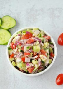 Top down shot of a small bowl with Greek salsa in it. Cherry tomatoes and slices of cucumber are to the side.