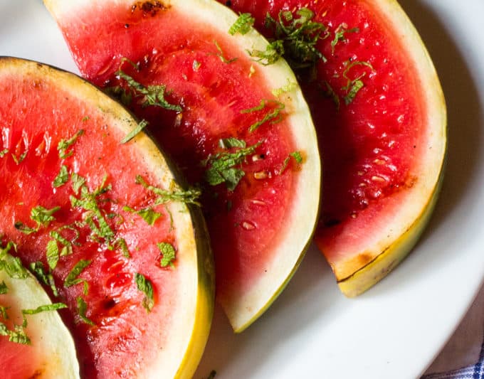 Close up of grilled watermelon slices with sliced mint on top, on a white platter.
