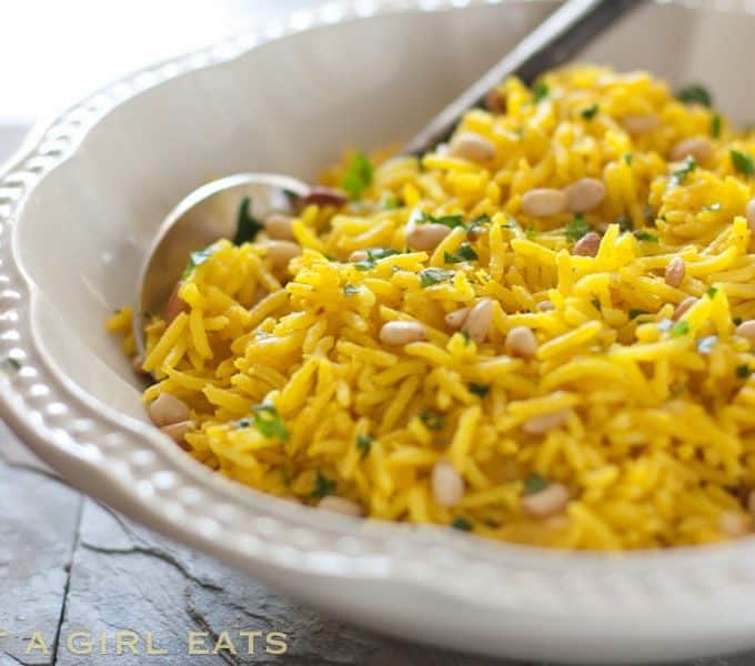 Close up of a yellow rice dish in a white bowl with a serving spoon in it.